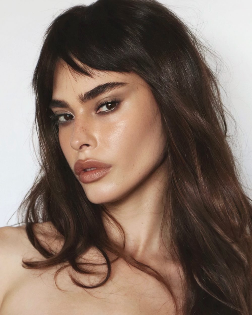 Close-up of a woman with dark brown hair, smoky eye makeup, and full lips looking to the left.