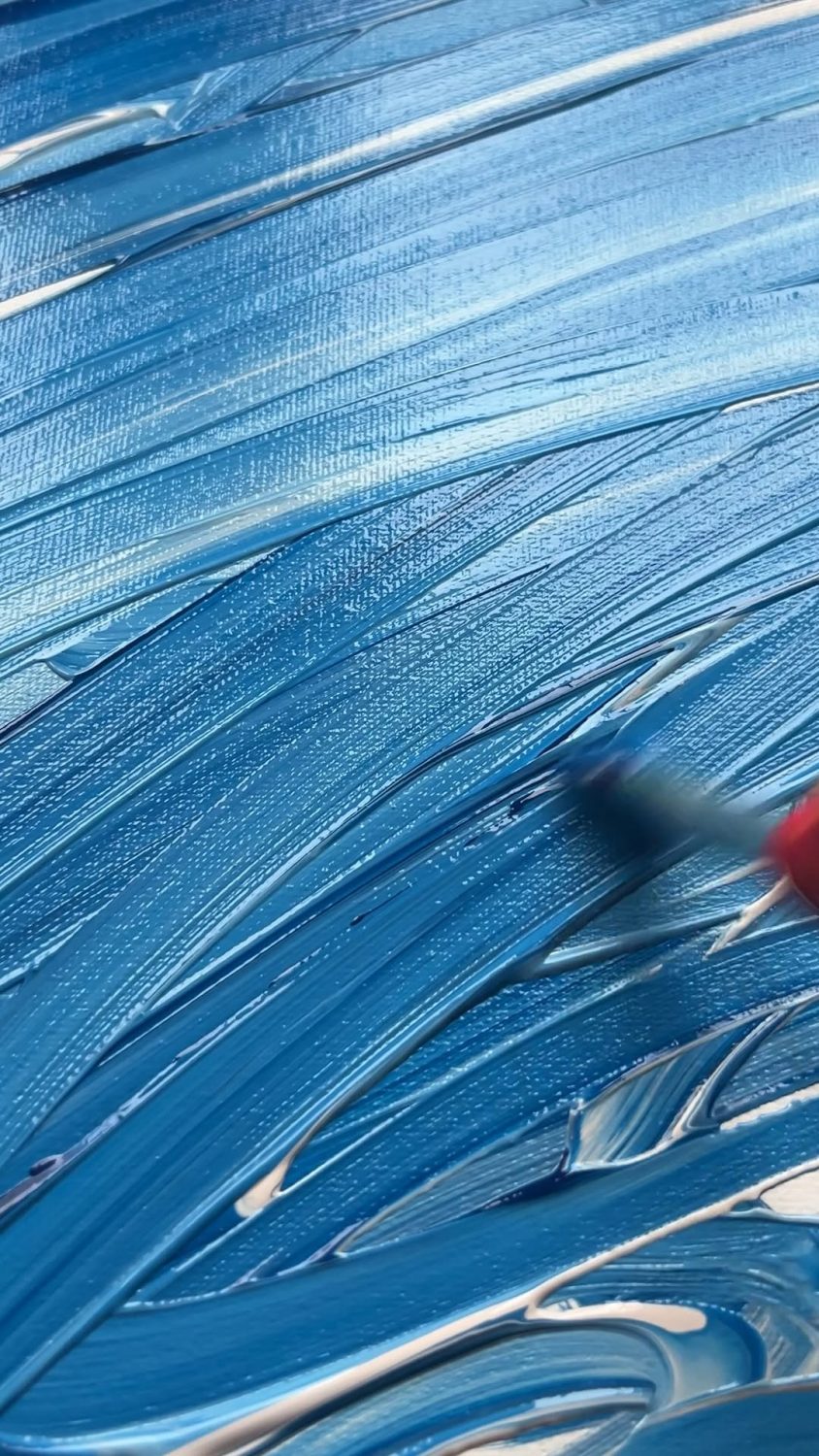 Blue acrylic paint being brushed in broad, sweeping strokes across a surface.