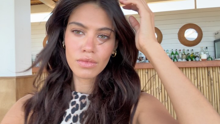 Woman taking a selfie at an outdoor bar, wearing a leopard print top with long dark hair.