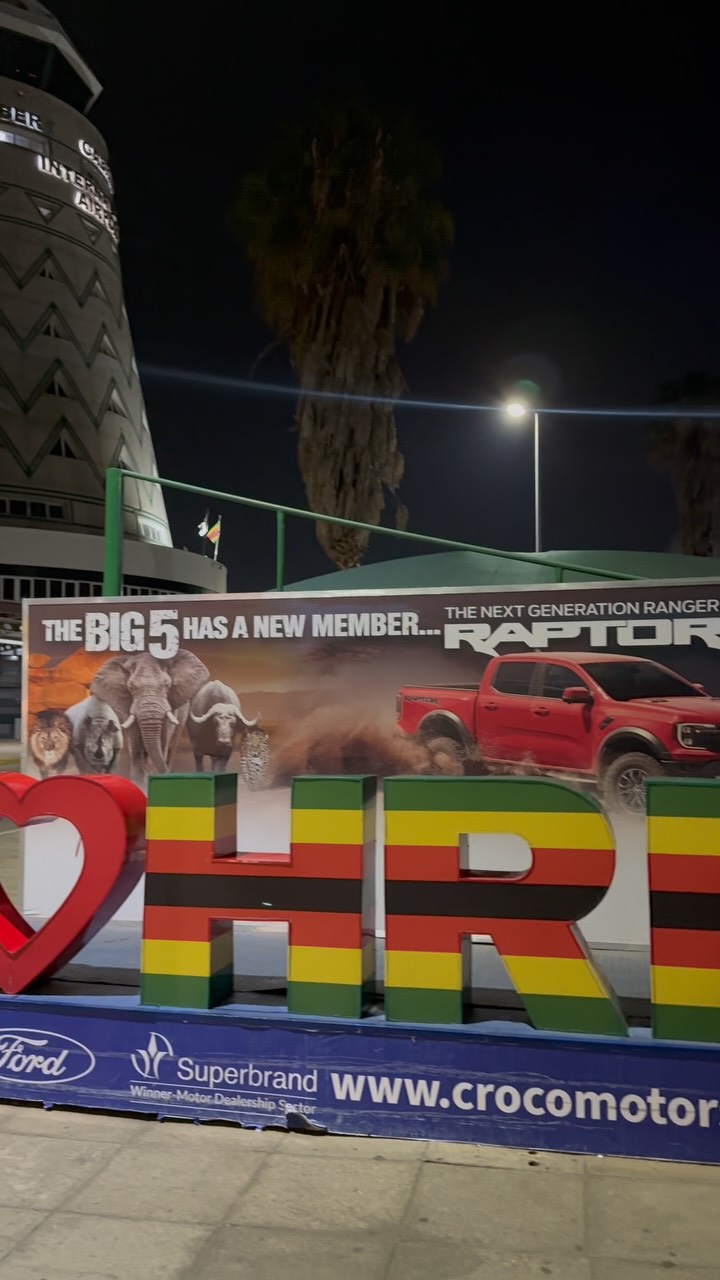 Nighttime outdoor promo board showing a red Ford Raptor pickup with wildlife imagery and large colorful letters in front.