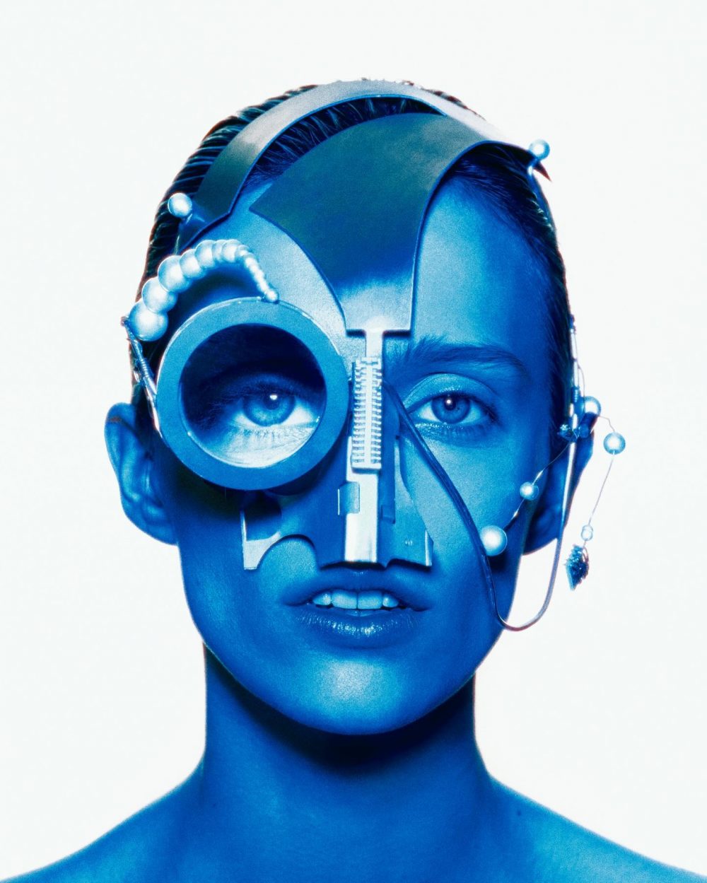 Close-up portrait of a person with blue-toned cybernetic headgear covering one eye, futuristic and sci-fi style.