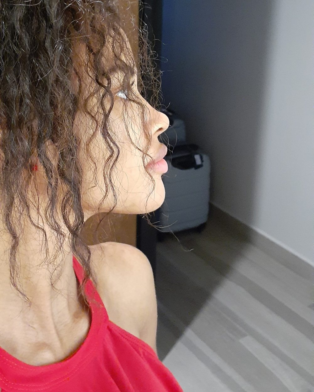 Profile of a person with curly hair wearing a red top, looking to the right indoors.