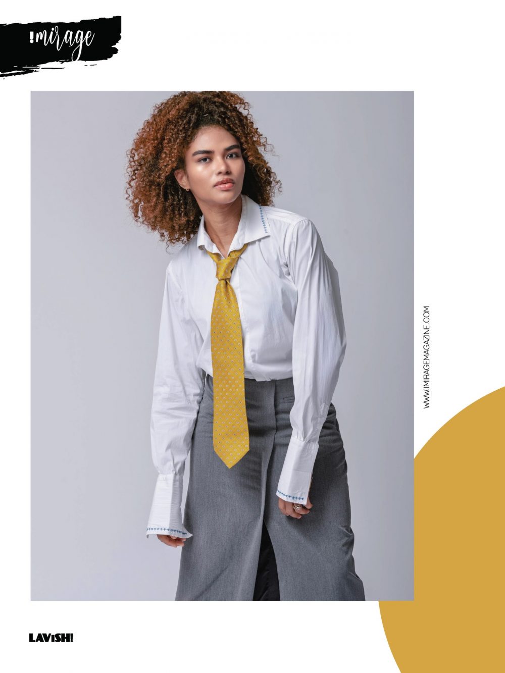 Model in a white shirt and yellow tie with gray trousers, posing against a light gray backdrop; fashion editorial image.