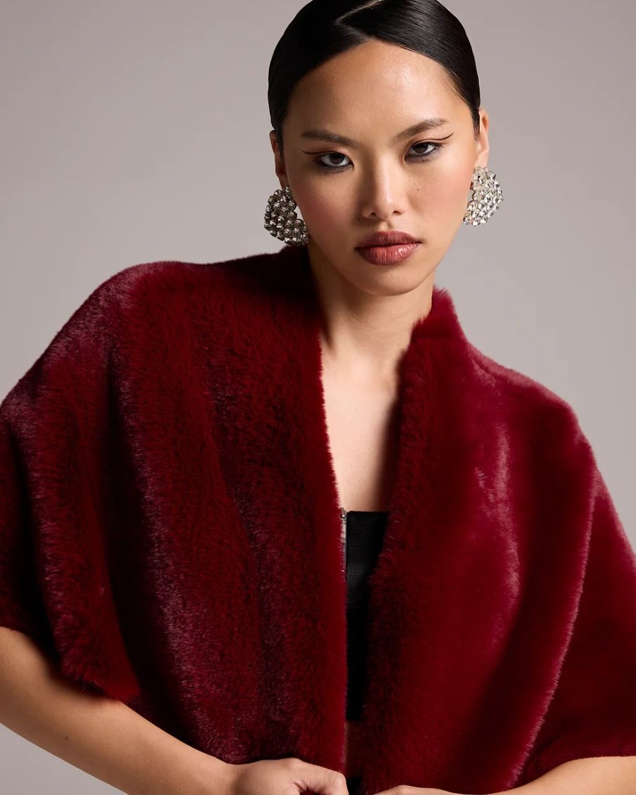 Woman wearing a deep red fur coat with large silver rhinestone earrings, looking confidently at the camera.