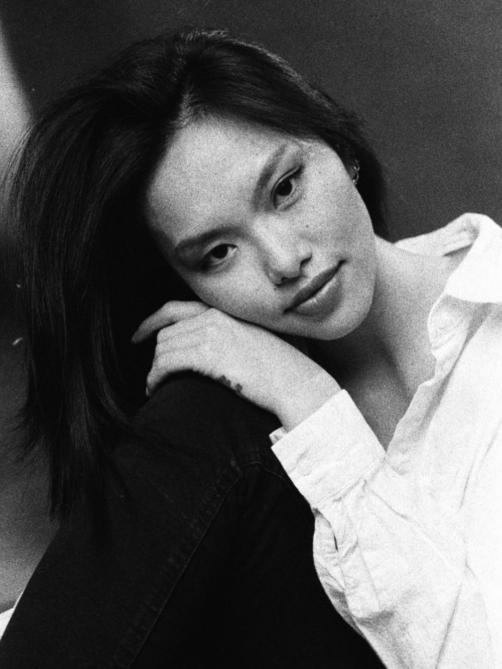 Black-and-white portrait of a woman resting her head on folded hands, looking softly downward.