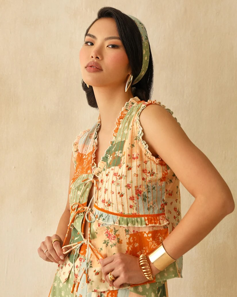 Woman posing in a pastel patchwork floral sleeveless top with a green headband and gold jewelry.