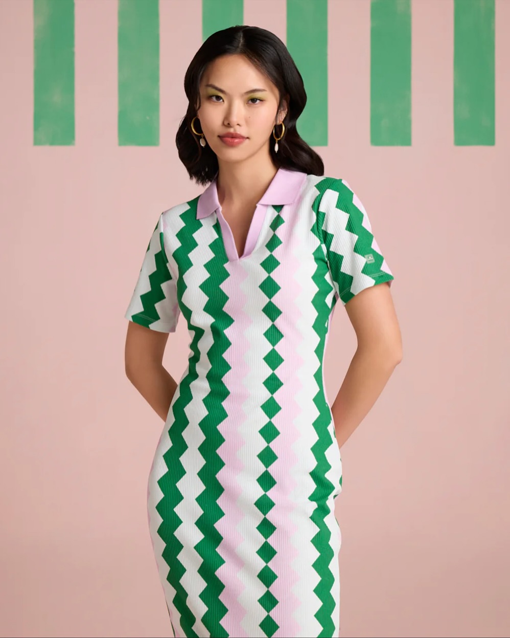 Young woman in a green and pink zigzag striped dress with a pink collar, posing with hands on her hips.