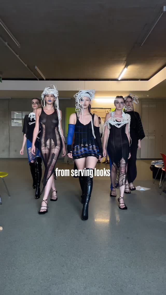 Five models walk a backstage runway in avant-garde black outfits with white sculptural headpieces; caption reads 'from serving looks'.