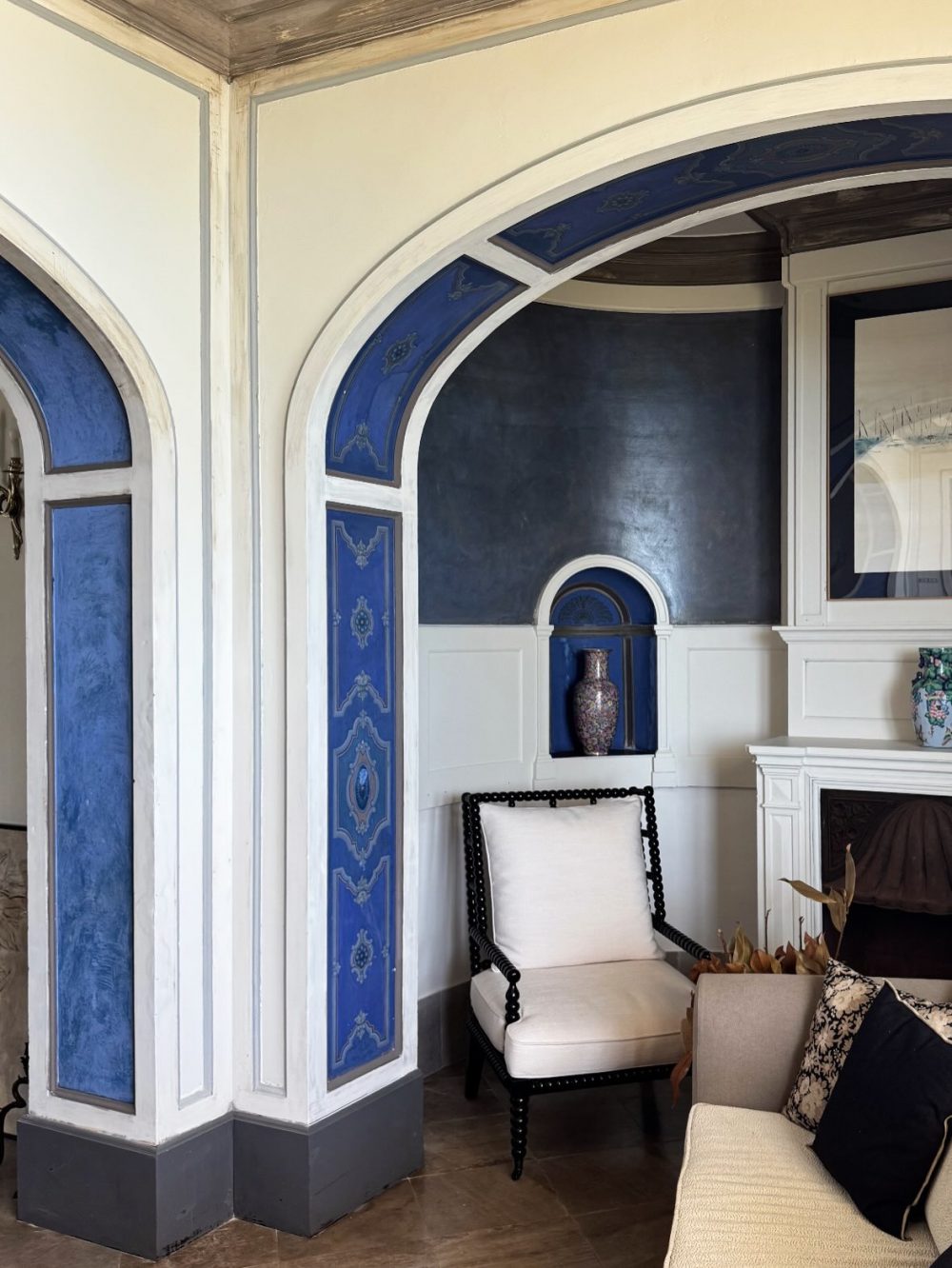 Blue-and-white arched alcove with decorative panels and a vase display, in a classic living room corner with a white cushioned chair nearby.