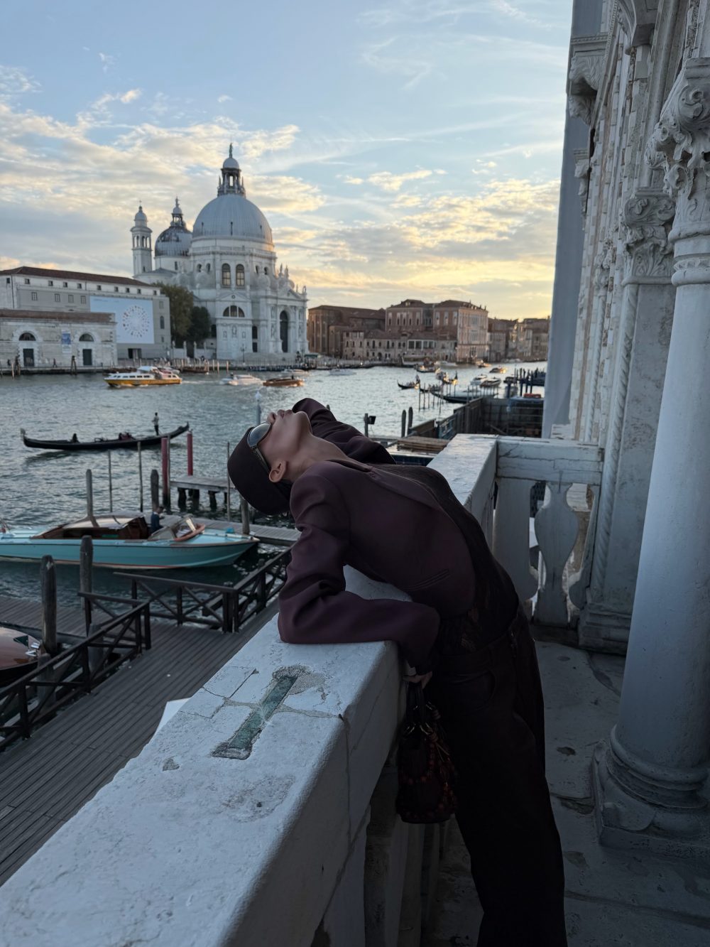 Person leaning on a white railing by a Venetian canal at sunset, with Santa Maria della Salute in the background.