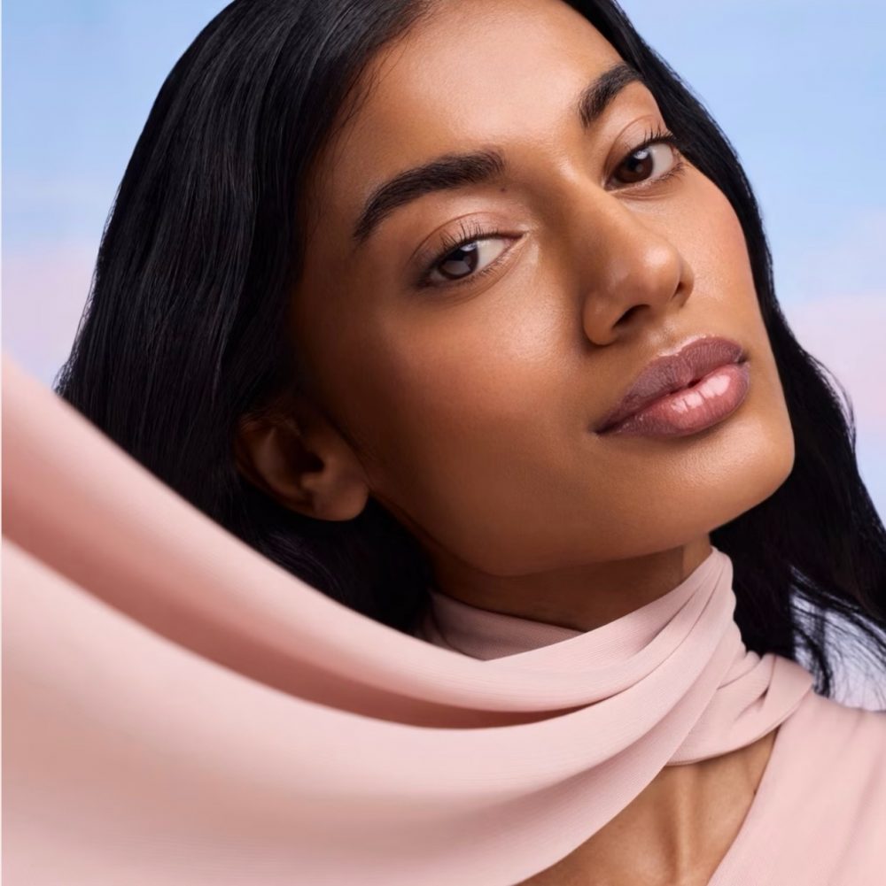 Close-up portrait of a woman with dark hair wearing a pale pink scarf, gazing softly at the camera.