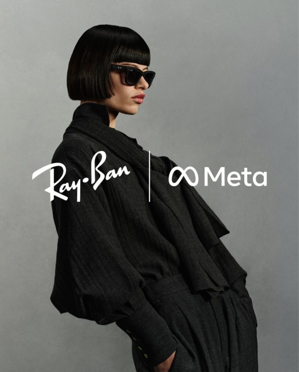 Model in a dark coat wearing black sunglasses, posing against a gray background for a Ray-Ban Meta campaign