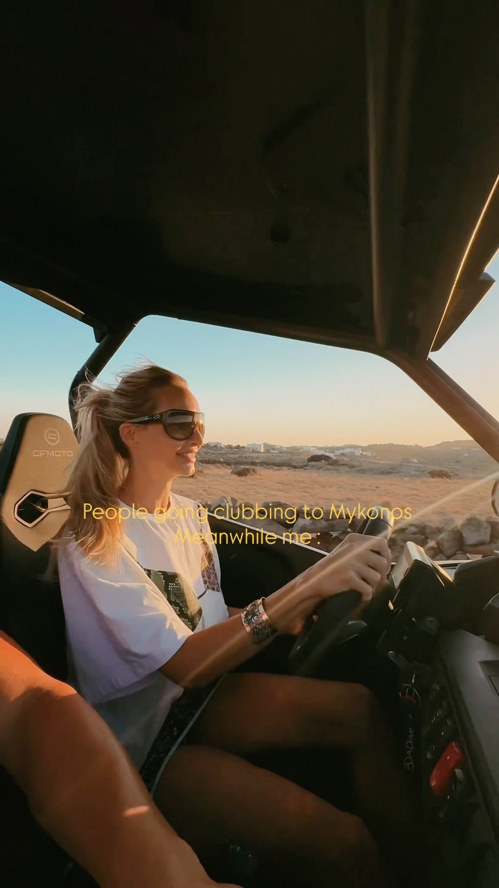 Woman in sunglasses smiles while driving a convertible at sunset along a desert/coastal road; the caption reads 'People going clubbing to Mykonos meanwhile me:'