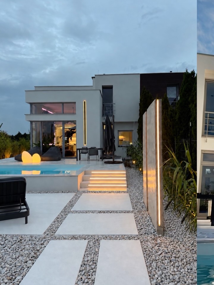 Modern backyard at dusk: rectangular pool, stepping-stone path on gravel, and a two-story house with warm-lit windows.