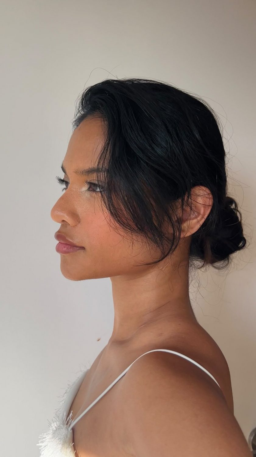 Profile view of a woman with dark hair in a low bun, wearing a white feather-strap top.