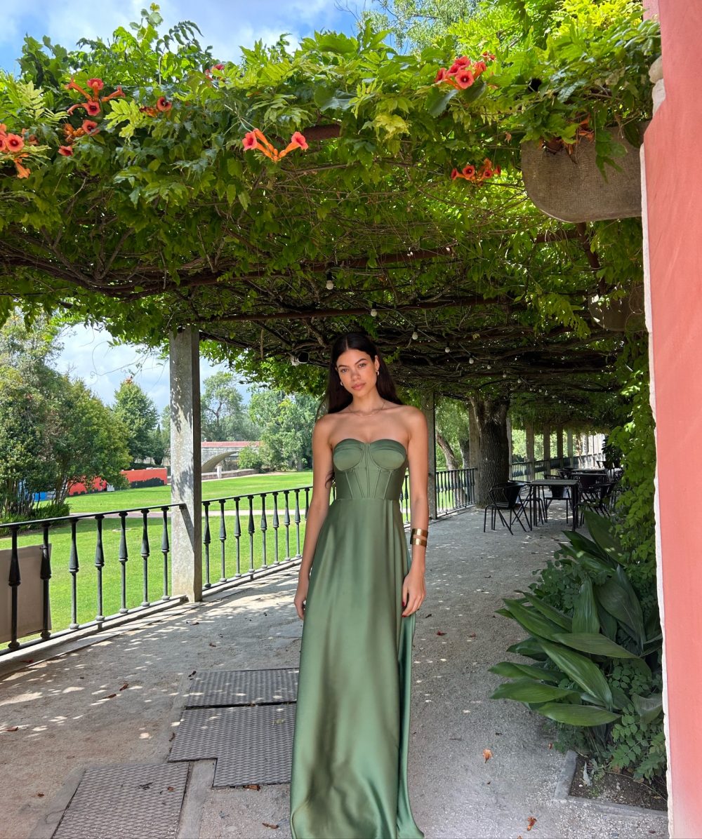 Woman in a strapless green gown stands under a vine-covered pergola with orange flowers in bloom.