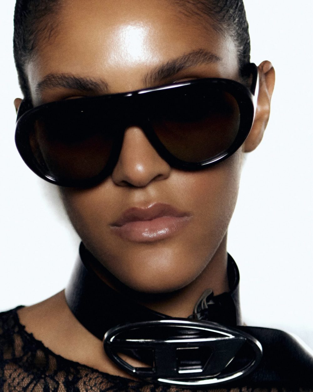 Close-up of a person wearing oversized black sunglasses, glossy lips, and a lace top with a black choker visible at the neck.