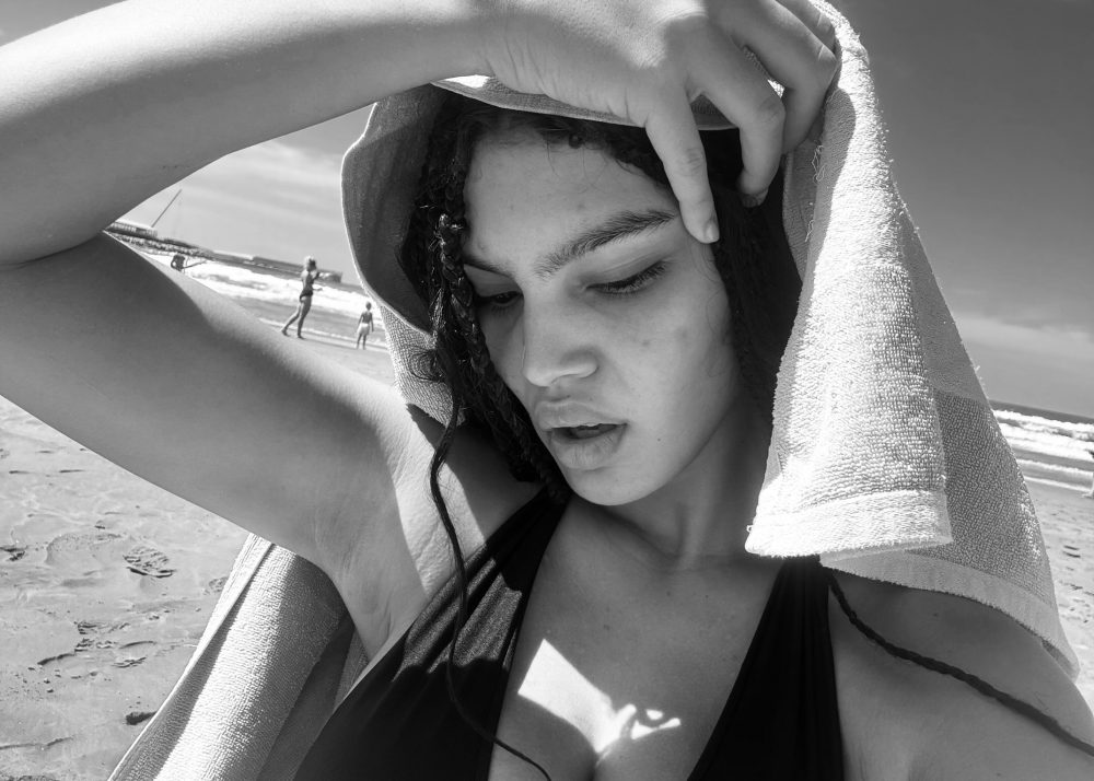 Close-up of a person at the beach with a towel wrapped around their head, eyes closed.